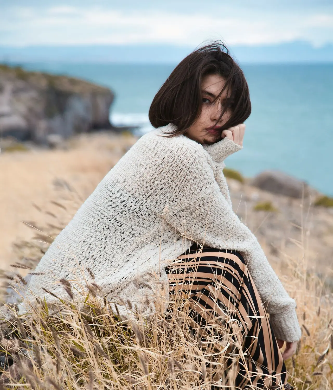 woman in white knit sweater sitting on brown grass field during daytime